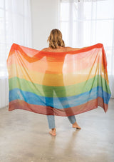 [Color: Rainbow] A model wearing a rainbow printed mesh scarf with a raw edge hem. 