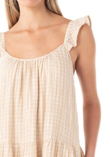 [Color: Natural] A close up front facing image of a blonde model wearing a casual bohemian mid length dress in a natural cotton seersucker check print. With adjustable ruffle straps, a scoop neckline in the front and back, side pockets, and a tiered flowy silhouette.