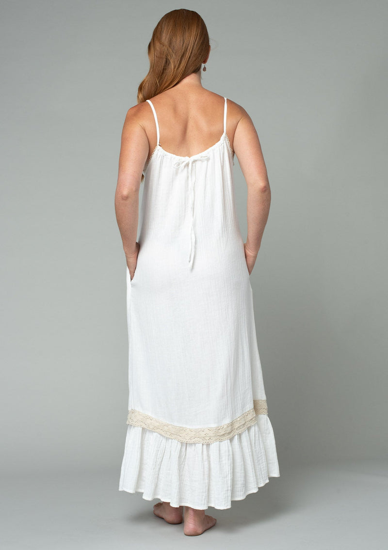 [Color: Off White/Natural] A full body back facing image of a red headed model wearing an off white cotton gauze sleeveless maxi dress with a natural crochet trim top and hemline. With adjustable spaghetti straps and a flowy fit.
