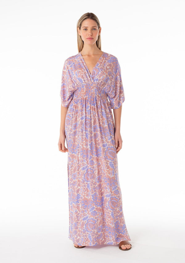 [Color: Ivory/Coral] A front facing image of a blonde model wearing a best selling resort bohemian maxi dress in a purple and coral pink retro floral print. With short kimono sleeves, a surplice v neckline, a smocked elastic waist, and an open back with tie closure. 