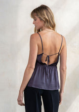 [Color: Gunmetal] A model wearing an elevated grey silky camisole with strappy back detail. With a v neckline, adjustable spaghetti straps, and a flattering relaxed silhouette.