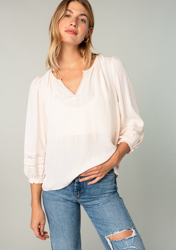 [Color: Almond] A front facing image of a blonde model wearing a light pink classic bohemian peasant top with voluminous lace trimmed long sleeves.