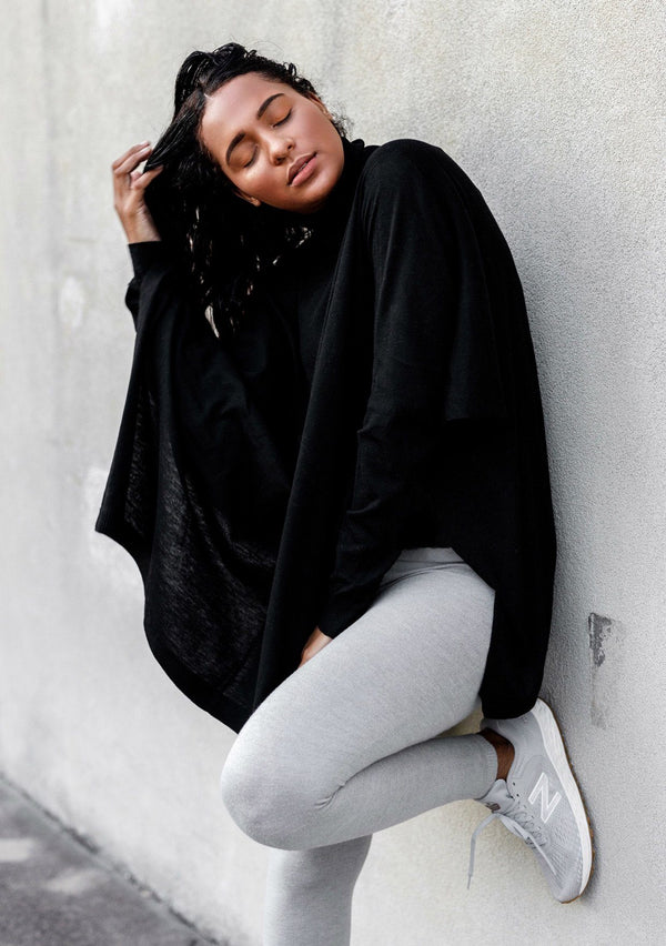 [Color: Black] A woman standing outside wearing a turtleneck sweater poncho. Featuring a flattering draped silhouette, breezy side vents, and a slightly longer tunic style length.