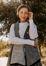 [Color: Black/OffWhite] Beautiful model wearing an effortlessly chic blanket style shawl vest with checkered and argyle patchwork details. Sweater vest shawl is black and white and extra soft.