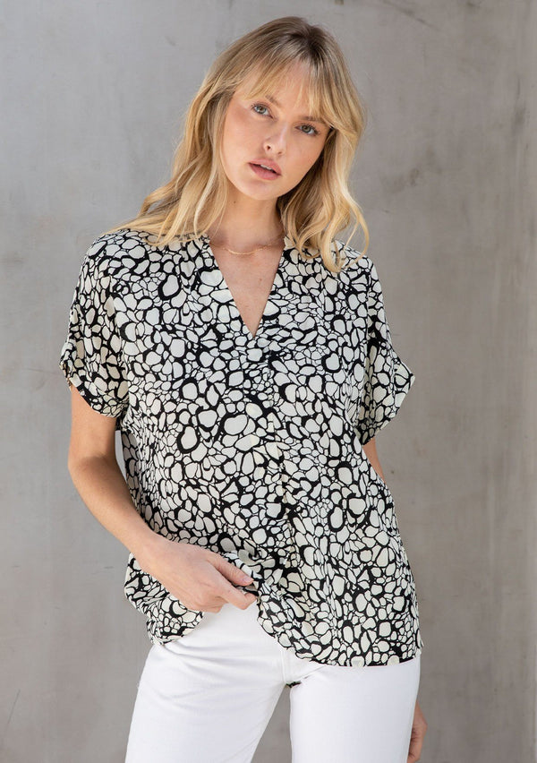 [Color: Natural/Black] A model wearing a lightweight cuffed sleeve top in an abstract black circles print. With an easy popover silhouette, perfect for work or play. 