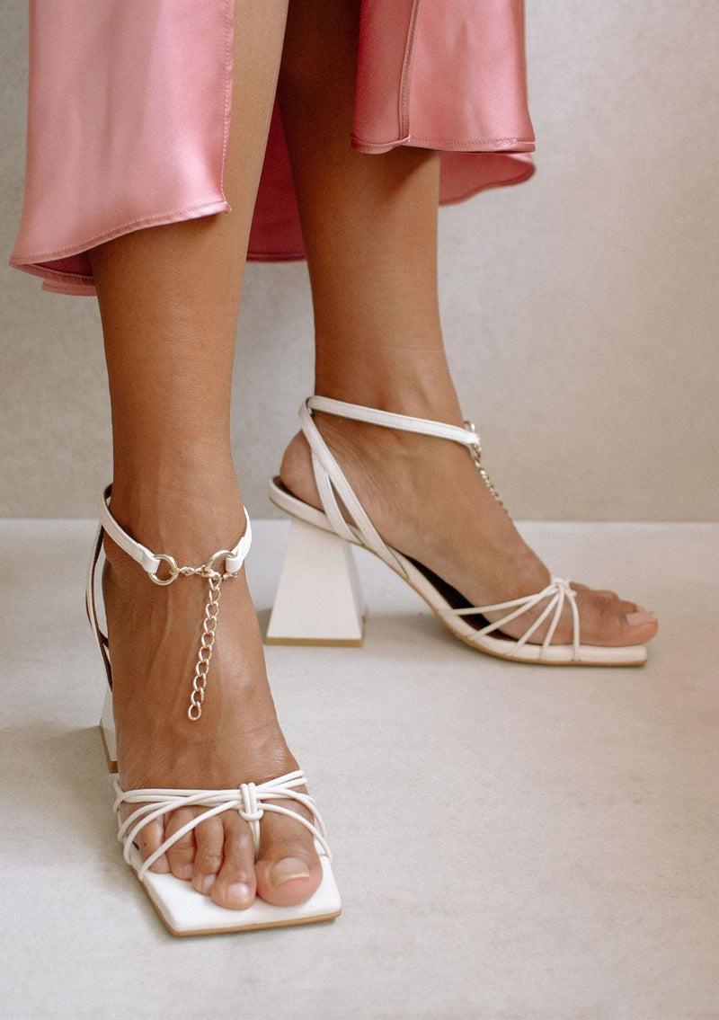 [Color: Off White] Alohas chic and trendy white leather strap block heeled sandal. With a delicate front chain accent and pyramid shaped heel with notched cutout. 