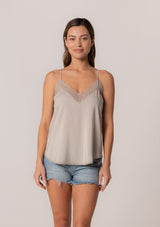 [Color: Mink] A front facing image of a brunette model wearing a light brown camisole tank top. With spaghetti straps, a v neckline, lace trim, a racerback, and a relaxed fit. 