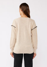 [Color: Oatmeal/Black] A brunette model wearing an everyday sweater with a relaxed silhouette in a beige tan. With a classic v neckline, long sleeves, and an exposed seam with blanket stitch. A fall sweater styled with black bottom and casual sandals. 