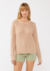 [Color: Truffle] A front facing image of a blonde model in an orange-tan pointelle cable knit sweater with long sleeves, a round neckline, and ribbed trim—a lightweight, breezy layer ideal for casual days, resort looks, or cozy beach mornings.