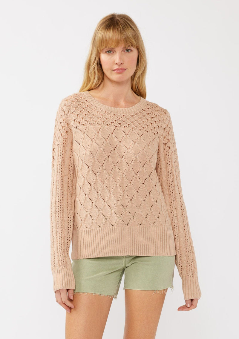 [Color: Truffle] A front facing image of a blonde model in an orange-tan pointelle cable knit sweater with long sleeves, a round neckline, and ribbed trim—a lightweight, breezy layer ideal for casual days, resort looks, or cozy beach mornings.