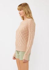 [Color: Truffle] A side facing image of a blonde model in an orange-tan pointelle cable knit sweater with long sleeves, a round neckline, and ribbed trim—a lightweight, breezy layer ideal for casual days, resort looks, or cozy beach mornings.