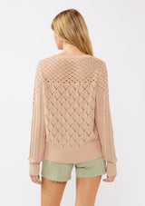 [Color: Truffle] A back facing image of a blonde model in an orange-tan pointelle cable knit sweater with long sleeves, a round neckline, and ribbed trim—a lightweight, breezy layer ideal for casual days, resort looks, or cozy beach mornings.