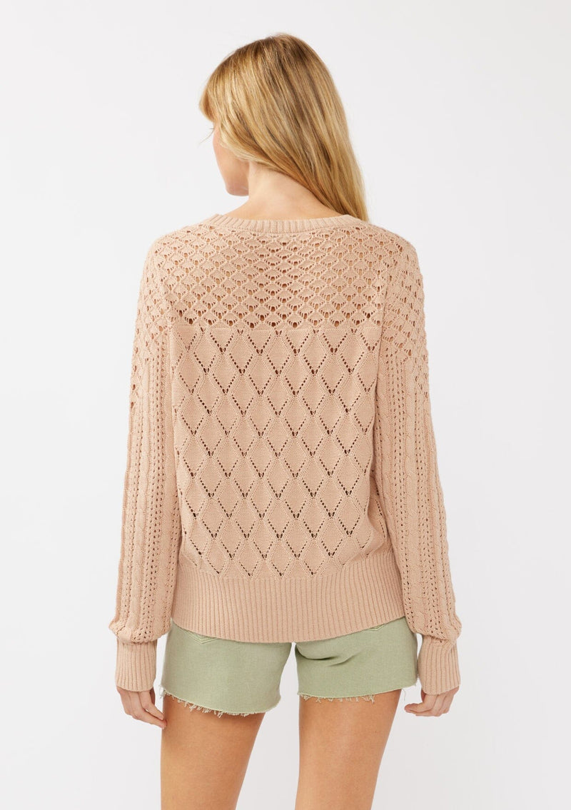 [Color: Truffle] A back facing image of a blonde model in an orange-tan pointelle cable knit sweater with long sleeves, a round neckline, and ribbed trim—a lightweight, breezy layer ideal for casual days, resort looks, or cozy beach mornings.