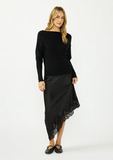 [Color: Black] A front facing image of a blonde model wearing a black pullover sweater with a boat neckline and long sleeves that taper at the cuffs. Styled with a black satin lace skirt. 
