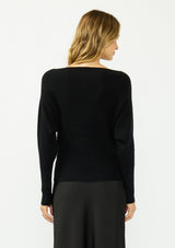 [Color: Black] A back facing image of a blonde model wearing a black pullover sweater with a boat neckline and long sleeves that taper at the cuffs. Styled with a black satin skirt. 
