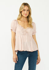 [Color: Dusty Rose] A front facing image of a blonde model wearing a pink satin jacquard puff sleeve top with lace trim and a tie front detail. 