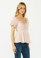 [Color: Dusty Rose] A side facing image of a blonde model wearing a pink satin jacquard puff sleeve top with lace trim and a tie front detail. 
