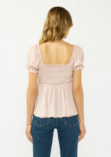 [Color: Dusty Rose] A back facing image of a blonde model wearing a pink satin jacquard puff sleeve top with lace trim and a tie front detail. 