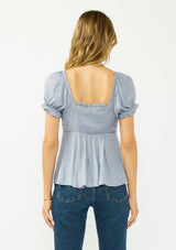 [Color: Dusty Blue] A back facing image of a blonde model wearing a blue satin jacquard puff sleeve top with lace trim and a tie front detail. 