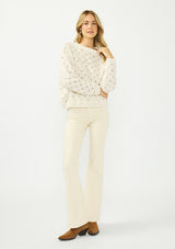 [Color: Natural] A front facing image of a blonde model wearing a cozy off white pointelle knit sweater with a crew neckline. 
