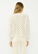 [Color: Natural] A back facing image of a blonde model wearing a cozy off white pointelle knit sweater with a crew neckline. 