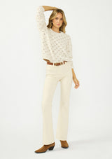 [Color: Natural] A front facing image of a blonde model wearing a cozy off white pointelle knit sweater with a crew neckline. Tucked into a beige denim with a brown belt. 