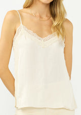 [Color: Champagne] A detail image of a blonde model wearing an ivory satin camisole with lace trim, adjustable spaghetti straps, and side slits. 