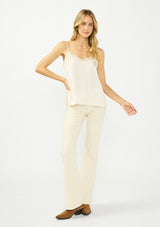 [Color: Champagne] A front facing image of a blonde model wearing an ivory satin camisole with lace trim, adjustable spaghetti straps, and side slits. 