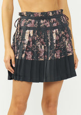 [Color: Grey/Dusty Rose] A front facing image of a grey floral pleated skirt with a satin hem, clipped lurex, paperbag waist, and side tie details. 