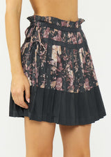 [Color: Grey/Dusty Rose] A side facing image of a grey floral pleated skirt with a satin hem, clipped lurex, paperbag waist, and side tie details. 