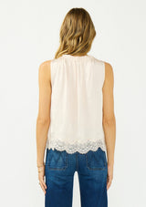 [Color: Petal] A back facing image of a blonde model wearing an light pink poly satin tank top with a ruffled v neckline, tie front, button front, and a lace trim hem. 