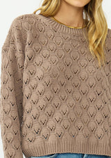[Color: Mocha] A detail image of a blonde model wearing a cozy brown pointelle knit sweater with a crew neckline. Styled with a light wash denim. 