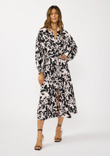 [Color: Vanilla/Black] A front facing image of a brunette model wearing an abstract floral print maxi dress with long dolman sleeves, a v-neckline, and long waist ties tied to the front. Complete with a chic front slit for movement