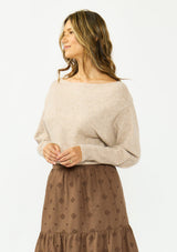 [Color: Heather Light Taupe] A side facing image of a brunette model wearing a light brown pullover sweater with a boat neckline and ribbed cuffs. Styled with a brown embroidered skirt. 