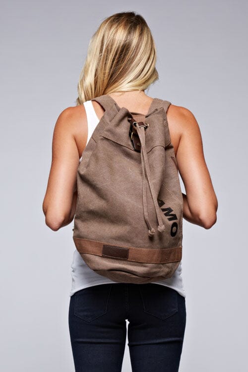 [Color: Khaki] A blonde model wearing a cotton blend khaki sack backpack with a drawstring closure. 