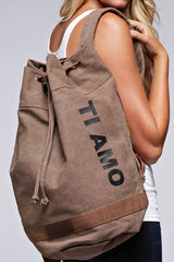 [Color: Khaki] A blonde model wearing a cotton blend khaki sack backpack with a drawstring closure. 