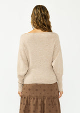 [Color: Heather Light Taupe] A back facing image of a brunette model wearing a light brown pullover sweater with a boat neckline and ribbed cuffs. Styled with a brown embroidered skirt. 