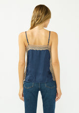 [Color: Navy/Taupe] A back facing image of a blonde model wearing a navy satin camisole with lace trim, adjustable spaghetti straps, and side slits. 