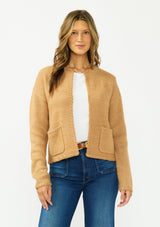 [Color: Camel] A front facing image of a brunette model wearing a camel brown cardigan with an open front, patch pockets, and blanket stitch trims. Styled over a white tee and dark wash denim. 