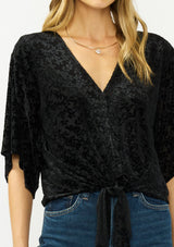 [Color: Black] A detail image of a blonde model wearing a black floral burnout tie front top with flowy half length sleeves and a v neckline. 