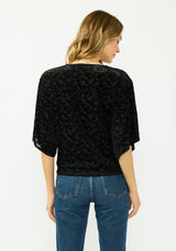 [Color: Black] A back facing image of a blonde model wearing a black floral burnout tie front top with flowy half length sleeves and a v neckline. 