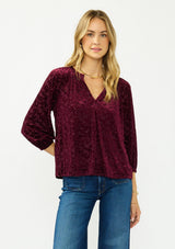 [Color: Merlot] A front facing image of a blonde model wearing a burgundy floral burnout blouse with a v neckline three quarter length sleeve. 