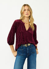 [Color: Merlot] A front facing image of a blonde model wearing a burgundy floral burnout blouse with a v neckline three quarter length sleeve. 