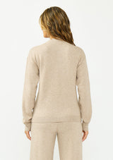 [Color: Heather Taupe] A back facing image of a brunette model wearing a beige v neck sweater with a cable knit detail and styled with a matching bottom. 