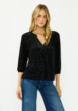 [Color: Black] A front facing image of a blonde model wearing a black floral burnout blouse with a v neckline and three quarter length sleeves.