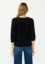 [Color: Black] A back facing image of a blonde model wearing a black floral burnout blouse with a v neckline and three quarter length sleeves.