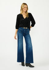 [Color: Black] A front facing image of a blonde model wearing a black floral burnout blouse with a v neckline and three quarter length sleeves. Styled tucked into a dark wash denim with a black belt. 
