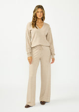 [Color: Heather Taupe] A woman modeling a matching beige knit loungewear set consisting of a long-sleeve V-neck top and wide-leg drawstring pants.