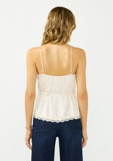 [Color: Antique Blush] A back facing image of a blonde model wearing a light pink poly satin lace trim top with  a button front, adjustable spaghetti straps, and a drawstring waist with tie detail. Paired with a classic dark wash denim. 