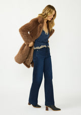 [Color: Mocha] A side facing image of a blonde model wearing a brown faux fur coat with a shawl collared neckline, and side pockets. A large fur coat for the winter, holidays, and other special occasions. 